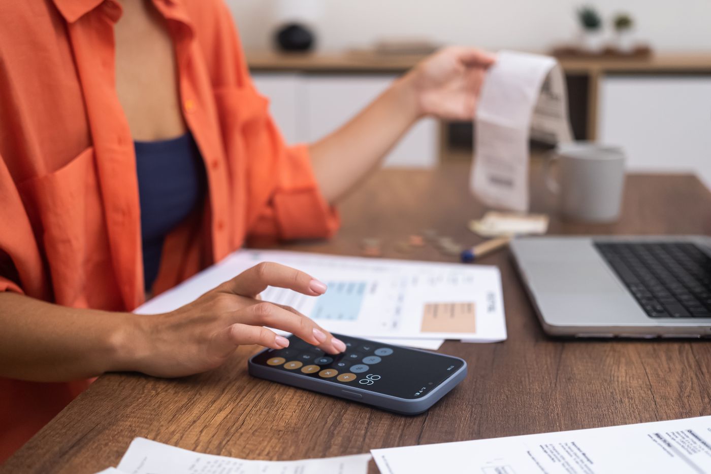 Laptop On The Desk, A Woman Skillfully Calculates Household Expenditures On Her Smartphone. - Auster Inteligência Contábil