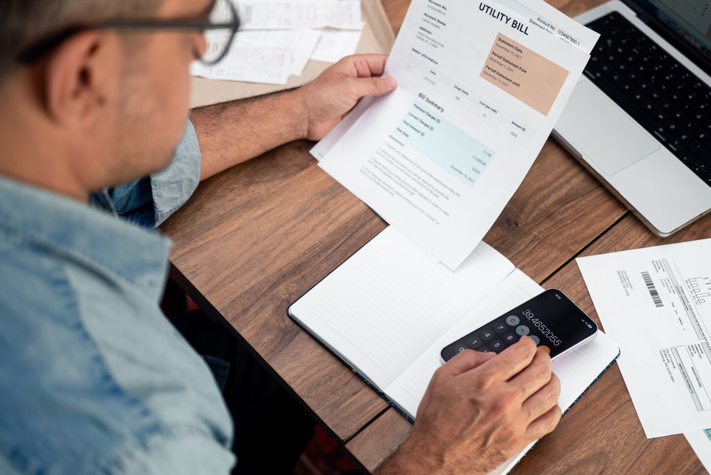 Mature Businessman Counts Sum Of Regular Payment For Utility Bills With Mobile App At Desk - Auster Inteligência Contábil