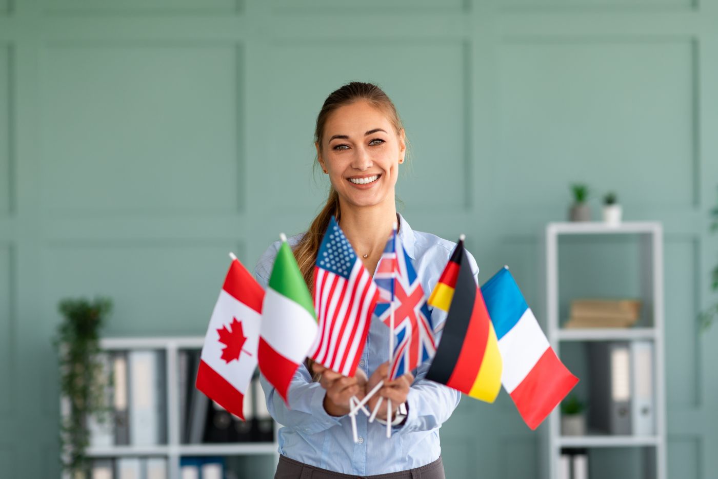 Happy Female Tutor Showing Bunch Of Diverse Flags, Recommending Foreign Language Studying School - Auster Inteligência Contábil