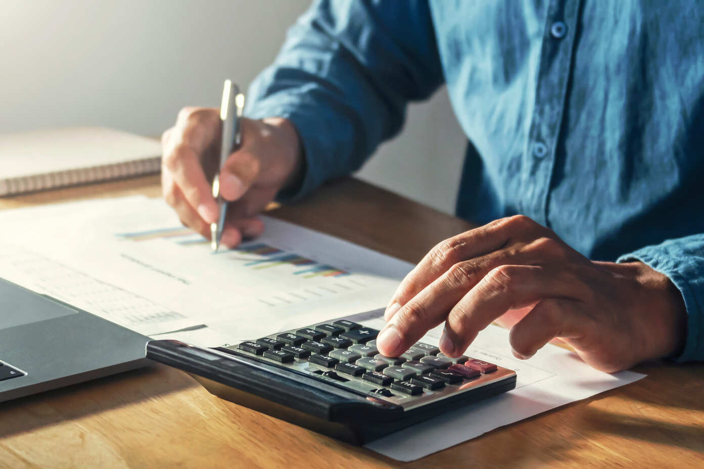 Imagem de um homem fazendo contas em uma calculadora com uma mão e segurando uma caneta na outra