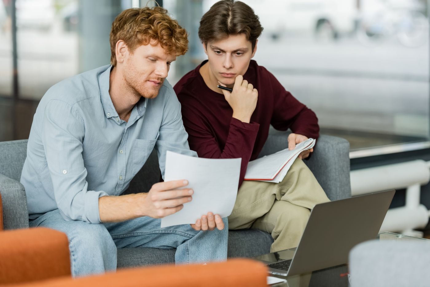 Two Men Focus On A Paper While Sitting On A Couch. - Auster Inteligência Contábil